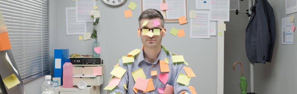 Office worker sitting at desk covered with colorful post it stick notes.